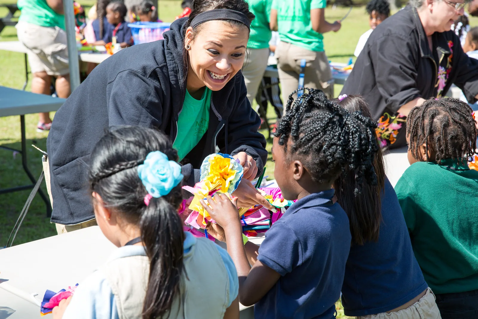 A volunteer helps children make paper flowers at a craft table during the Children's Festival at Park Circle in North Charleston.