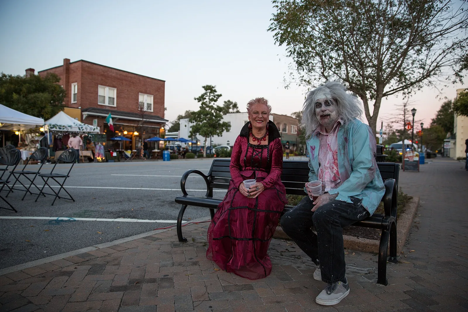 Two festivalgoers in Halloween costumes sit on a bench on East Montague Avenue during the North Charleston Harvest Festival.