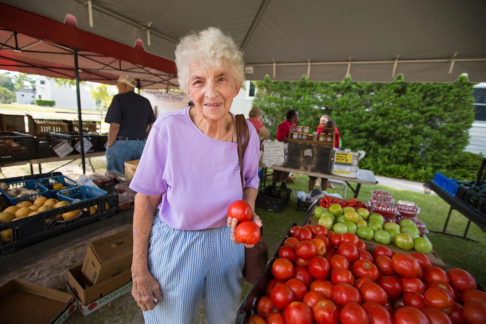 A shopper holds up tomatoes at a produce stand at the North Charleston Farmers Market.