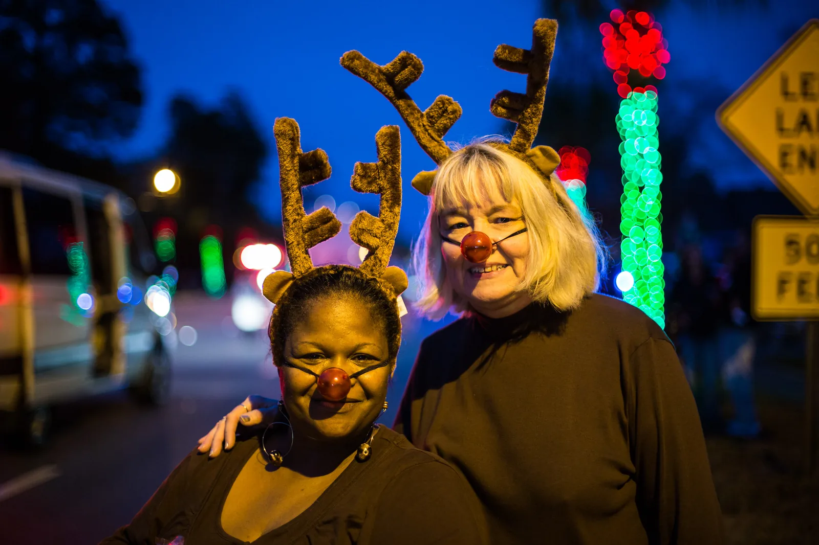 Two women in reindeer antlers and red noses stand beside lighted trees on Park Circle during North Charleston's Christmas Festival.