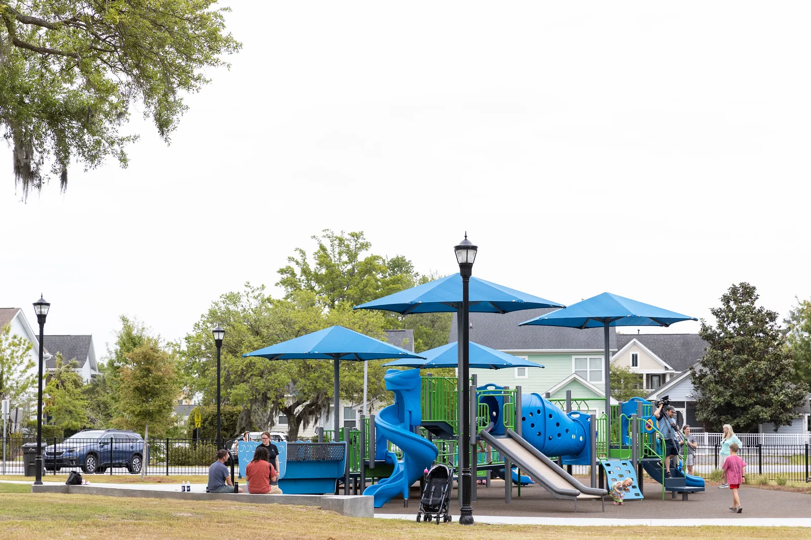 Children play under blue shade canopies at a North Charleston city playground with inclusive equipment.