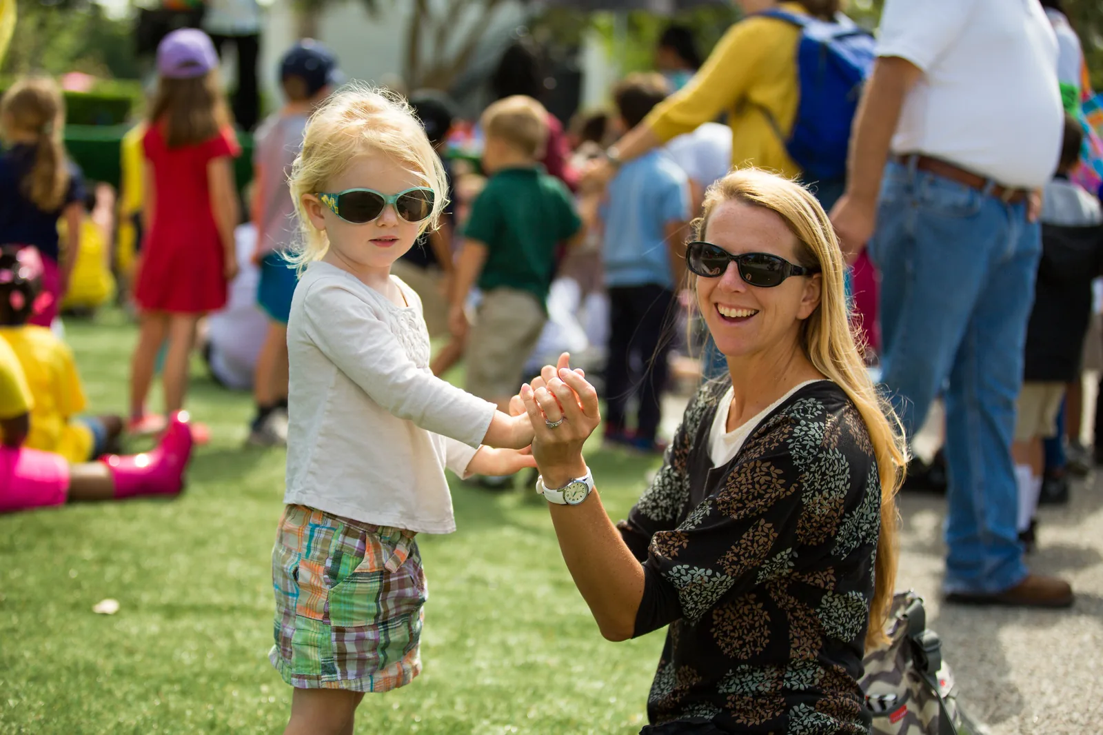 A mother and her young daughter in sunglasses hold hands on the lawn at the Children's Festival at Park Circle in North Charleston.
