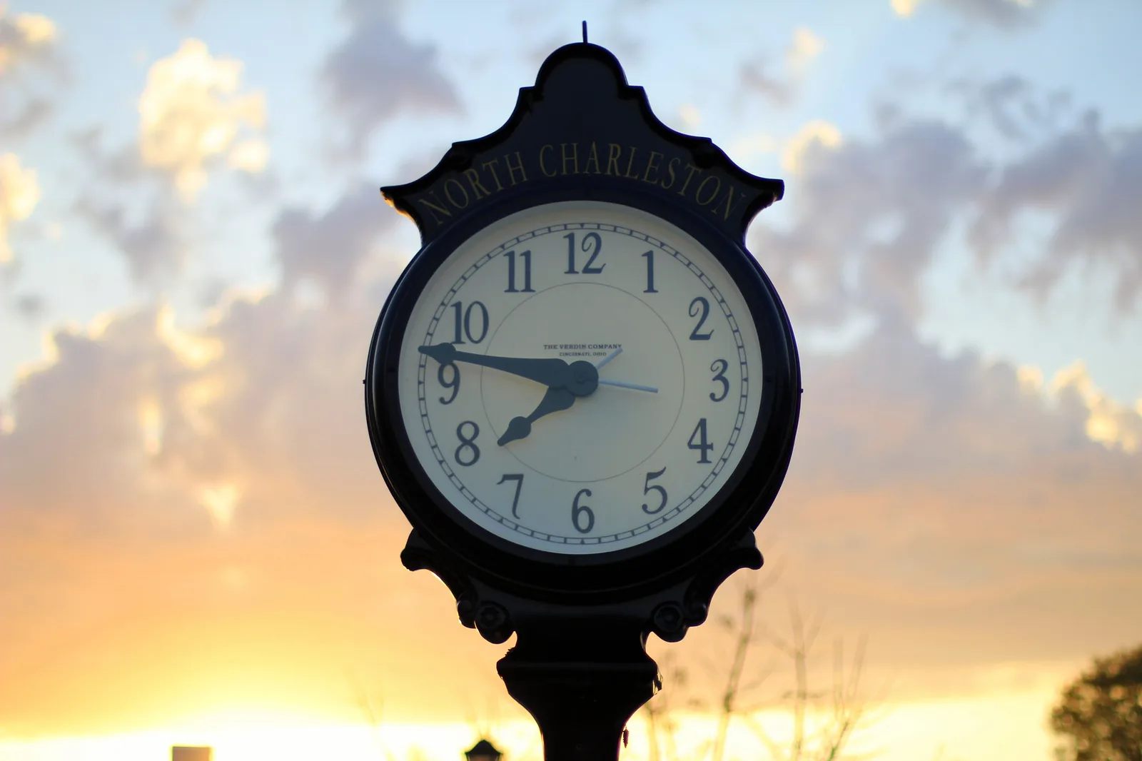 A street clock marked North Charleston stands against the sunset on East Montague Avenue in the Olde Village near Park Circle.