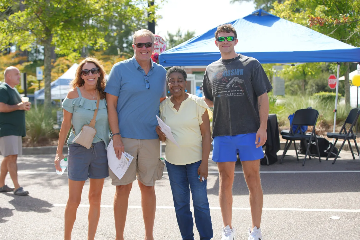 Four visitors stand together smiling among the vendor tents at Summerville Destination Market.