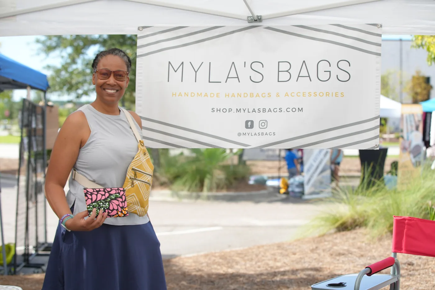 A woman holds a patterned bag in front of the Myla's Bags handmade handbags booth.