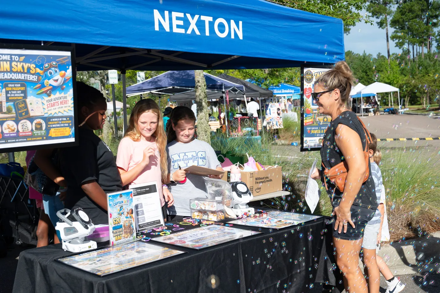 Children look at a display table under a blue Nexton tent at the market.